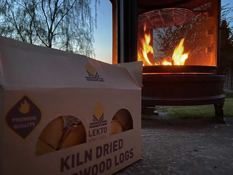 A Wood Burner At Dusk With a Box of Lekto Wood Fuels Kiln Dried Firewood in front of it