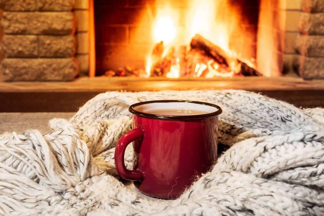 Red mug and cozy warm scarf in front of a fireplace in country house