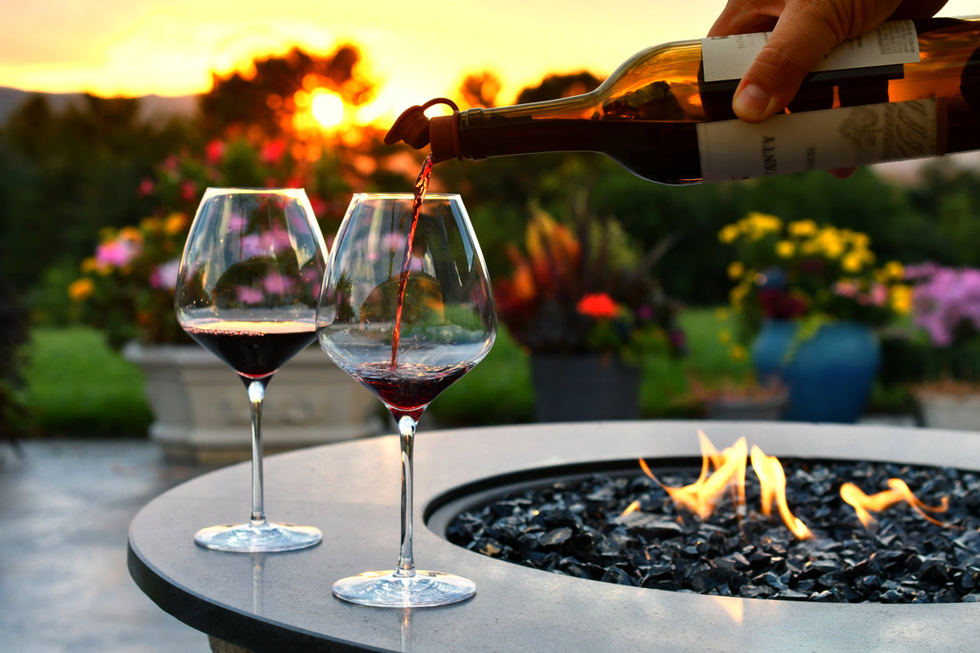 2 glasses of red wine on a lit fire pit garden table