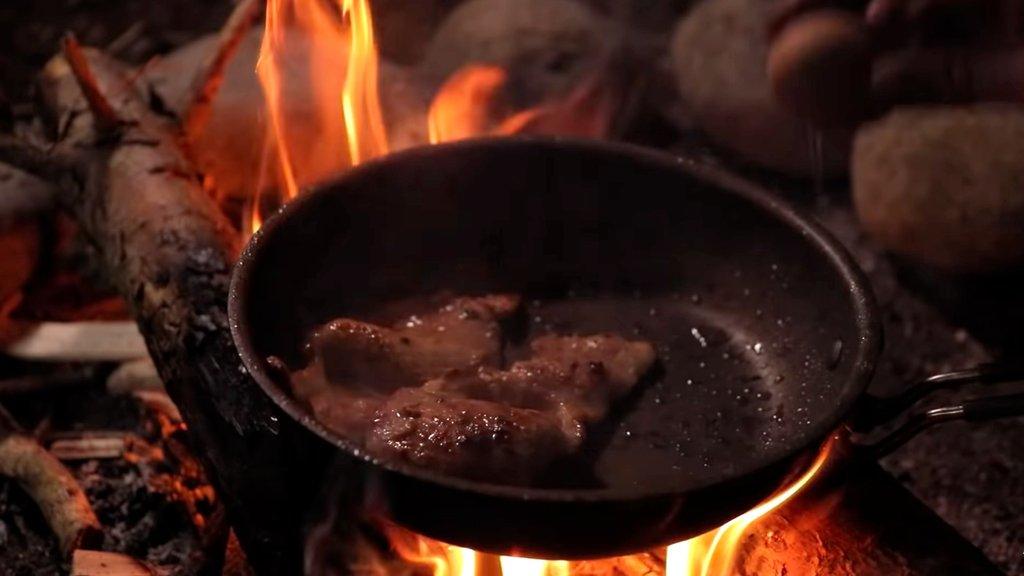 meat cooking in a pan on an open fire